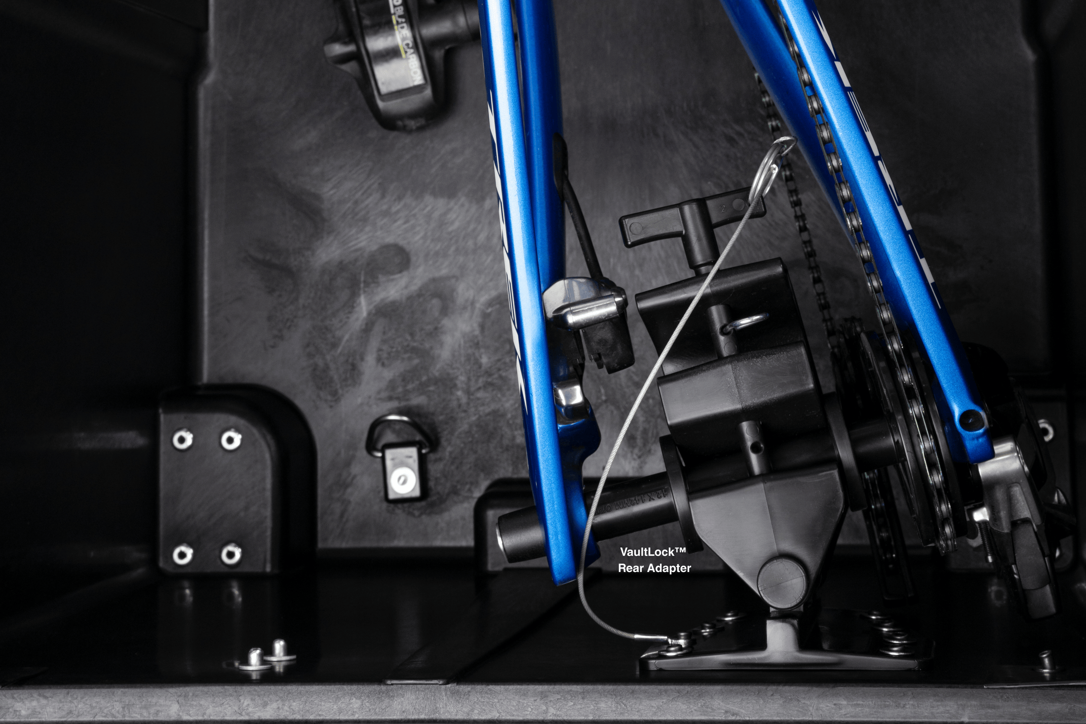 Close-up inside the case: a blue bike frame with its rear axle clamped into the VaultLock rear adapter, leaving the chain and derailleur clear.